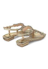 Sandalias metálicas doradas con una hebilla ancha adornada con strass, punta cuadrada y tacón bajo con un diseño en capas.