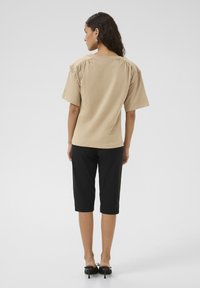 Beige top met korte mouwen, een relaxte pasvorm en geplooide schouderdetails, gecombineerd met zwarte cropped broek en zwarte hakken.