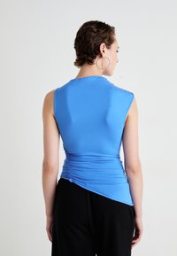 Top albastru fără mâneci cu un design elegant, având detalii plisate în spate și o margine asimetrică. Materialul pare neted și ușor.