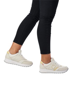 Leichte beigefarbene Sneakers mit weißen Sohlen, Gummiaußensohle, gelben Akzenten und Schnürverschluss. Texturiertes Obermaterial mit subtilen Designelementen.