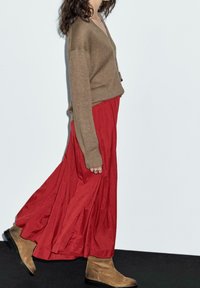 Ruskea neulottu V-paita yhdistettynä virtaavaan punaiseen maksihameeseen ja vaaleisiin mokkanahkasaappaisiin. Asussa on kerroksellisia tekstuureja ja värejä.