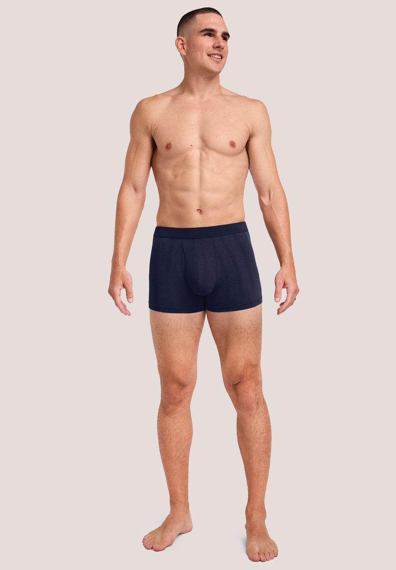 Boxer briefs de color azul marino hechos de una tela suave, que presentan una cinturilla cómoda y una abertura en la parte frontal, llevados por un modelo masculino.