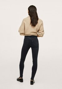 Jeans ajustados de mezclilla oscura con cintura alta, combinados con un suéter beige de gran tamaño, vistos desde atrás. Textura suave, diseño minimalista.