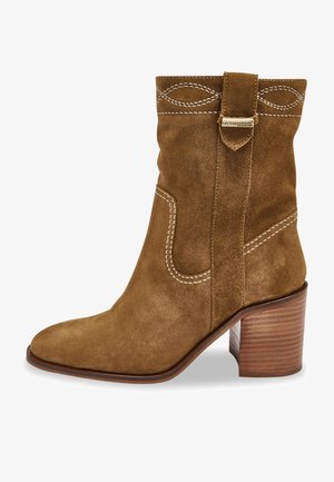 Botín de ante marrón hasta el tobillo con punta afilada, costuras decorativas en blanco, un diseño holgado y un tacón de madera apilada.