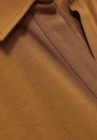 Bruine poloshirt met een zachte textuur, kraagontwerp en een netjes gestikte knoopsluiting. De stof lijkt lichtgewicht en soepel.