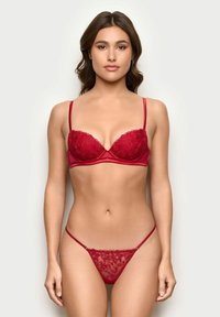 Sostén de encaje rojo con copas acolchadas y tirantes ajustables, combinado con un tanga de encaje transparente a juego que presenta un patrón floral y cobertura mínima.
