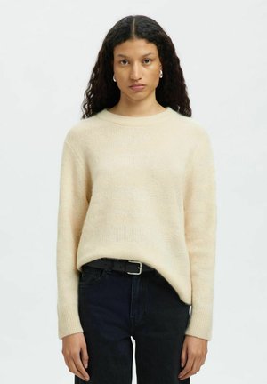 Kremfarvet, strikket sweater med løs pasform, subtile striber, rund halsudskæring og lange ærmer. Båret over mørke jeans med sort bælte.