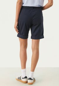 Marinblå bomullsshorts med uppvikta ärmar, som har en bakficka och en avslappnad passform, i kombination med vita strumpor och avslappnade sneakers.