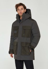 Mörkgrå isolerad parka med gröna accenter, stora framfickor och en dragkedjeförsedd bröstficka. Har en hög krage och justerbara ärmslut.