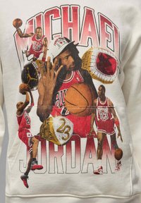 Valkoinen collegepaita, jossa on graafinen kuva Michael Jordanista Red Bulls -pelipaita päällään, koripalloja, mestaruussormuksia ja rohkeaa tekstiä.
