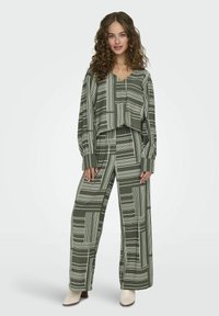 Completo a due pezzi in verde oliva, composto da un crop top e pantaloni a gamba larga. Il tessuto presenta un motivo a righe bianche geometriche, con una vestibilità comoda.