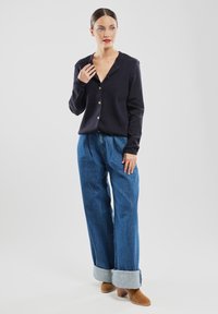 Granatowy kardigan z dekoltem w serek i pięcioma złotymi guzikami, zestawiony z jasnoniebieskimi szerokimi spodniami 3/4 z podwiniętymi nogawkami i beżowymi botkami na obcasie.