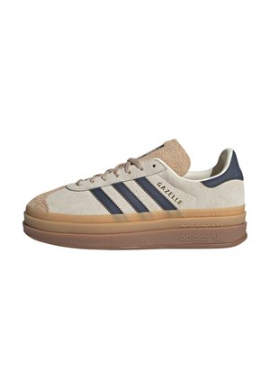 Adidas Gazelle sneakers har en beige suede-overdel, marineblå striber og en tyk gennemsigtig gummisål. Tungen er let polstret.
