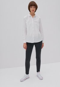 Camisa blanca de botones con cuello, pantalones ajustados oscuros y zapatillas blancas con acentos rojos. Textura de tela suave.