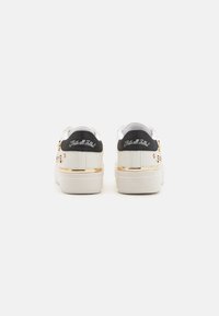 White sneakers with a black heel tab, gold accent on the sole, and decorative embellishments on the sides. Text on heel reads "That's all Folks!"