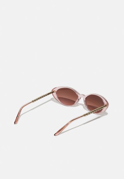 Pink sunglasses with round frames, brown tinted lenses, and gold-accented arms featuring a textured detail. Transparent pink plastic material.