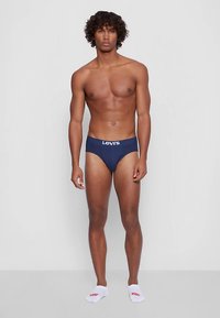 Sötétkék Levi's alsónadrág, fehér logós derékpánttal, testhez simuló fazonban, sima anyagból. A modellen fehér logós zoknik is vannak.