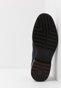 Chaussure en daim bleu marine avec une semelle en caoutchouc marron contrastante, dotée d'un motif de bande de roulement pour une meilleure adhérence. Le design comprend des perforations sur les côtés.