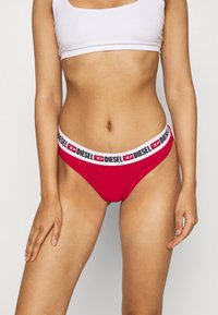 Bas de bikini rouge avec une ceinture élastique blanche portant la marque "DIESEL" en noir. Matière douce, design taille basse, texture lisse.