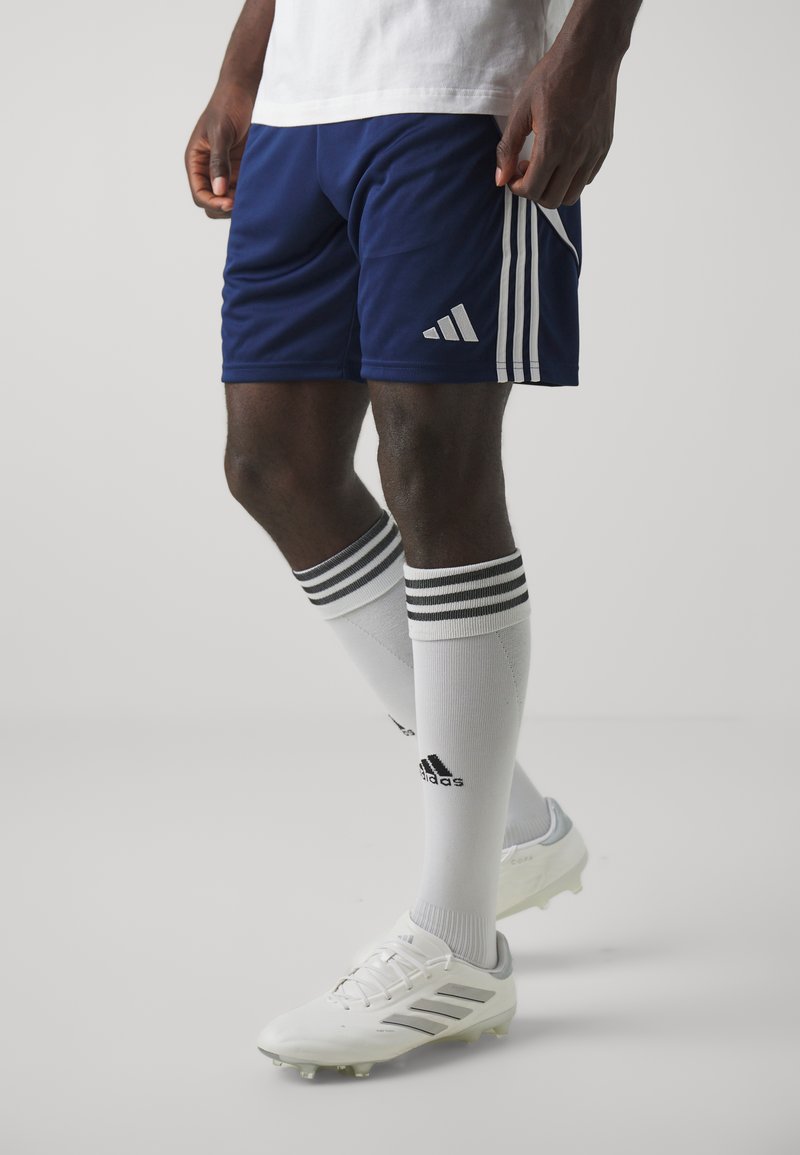 Plave atletske kratke hlače s bijelim prugama i Adidas logom, uparene s bijelim čarapama s crnim prugama i Adidas brandingom, te bijelim kopačkama.