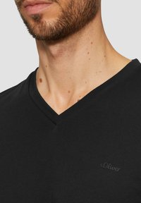 T-shirt nera a scollo a V realizzata in tessuto morbido, con un discreto logo s.Oliver sul petto. Vista ravvicinata che mette in evidenza il collo e la texture.