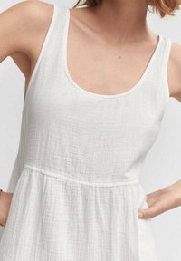 Abito bianco senza maniche realizzato in tessuto leggero e stropicciato. Presenta un collo rotondo e dettagli arricciati in vita.