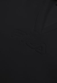 Tissu noir avec logo FILA discrètement embossé et un design à col en V.