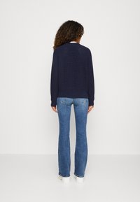 Maglione lavorato a maglia blu navy con orlo e polsini a coste, abbinato a jeans flare azzurri. La vista posteriore mostra il motivo a maglia e la vestibilità casual.