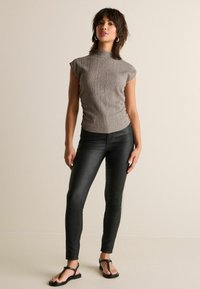Ljust grå, figurnära topp med korta ärmar och texturerad tyg; kombinerad med svarta, blanke leggings och svarta platta sandaler.