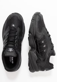 Svarta träningsskor med nät- och syntetöverdrag. Rund tå, vadderad krage, snörningsdesign och texturerad gummisula. Tre ränder som accent.