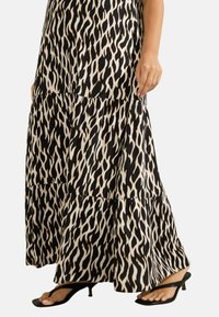 Svart och beige maxikjol med ett vågigt mönster, med tierade lager och en flödande siluett. Kombineras med svarta klacksandaler.