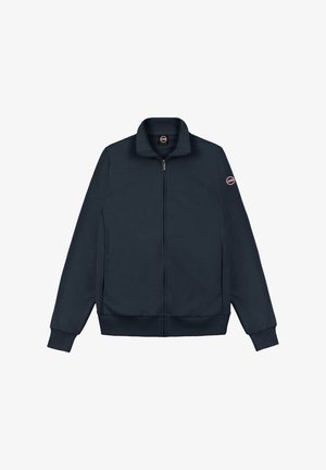 Chaqueta azul marino con cremallera, cuello alto, puños y bajo acanalados, y una parche redondo con logo en la manga izquierda.