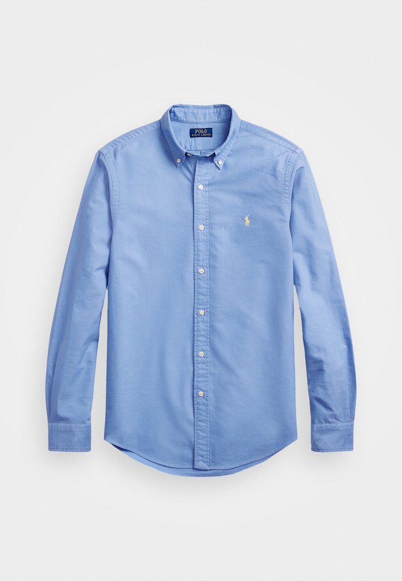 Light blue button-down shirt made of cotton with a collar, long sleeves, and a curved hem. Features a small embroidered logo on the chest.