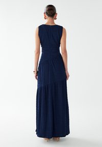 Maxikleid in Marineblau aus strukturiertem Stoff, ärmelloses Design, tailliertes Oberteil und ausgestellter Saum mit geometrischen Nahtdetails.