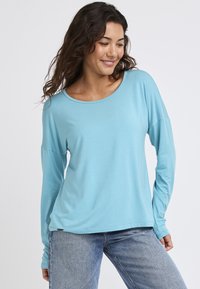 Jasnoniebieska koszula z długim rękawem o okrągłym dekolcie, miękka w dotyku i luźna, zestawiona z dżinsami o klasycznym kroju.