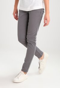 Pantalones ajustados gris de mezcla de algodón, con textura suave y bolsillos frontales, combinados con zapatillas blancas.