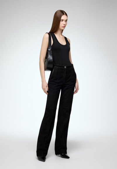 Zwarte suède wijde broek met contrasterende witte stiksels, gecombineerd met een fitted zwarte tanktop en een zwarte schoudertas.