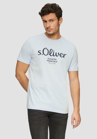 Heledsinine puuvillane T-särk lühikeste käiste ja ümarat kaelusega, millel on tume navy tekst: "s.Oliver Elevated Essentials alates 1969."