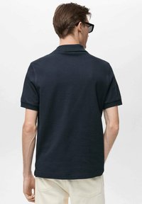 Námořnická polo košile s přehnutým límečkem, krátkými rukávy a jednoduchým designem. Tkanina vypadá hladce a jemně, má klasický střih.