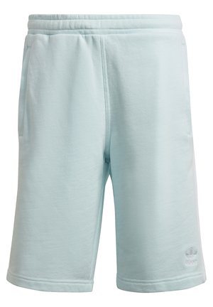 Homme portant un short bleu clair avec des bandes latérales, un t-shirt blanc et des baskets blanches, une main dans la poche, en posture de marche.