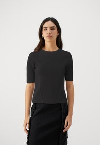 Black short-sleeve top with a fitted design, textured fabric, round neckline, and seams shaping the bodice; paired with a frayed black skirt.