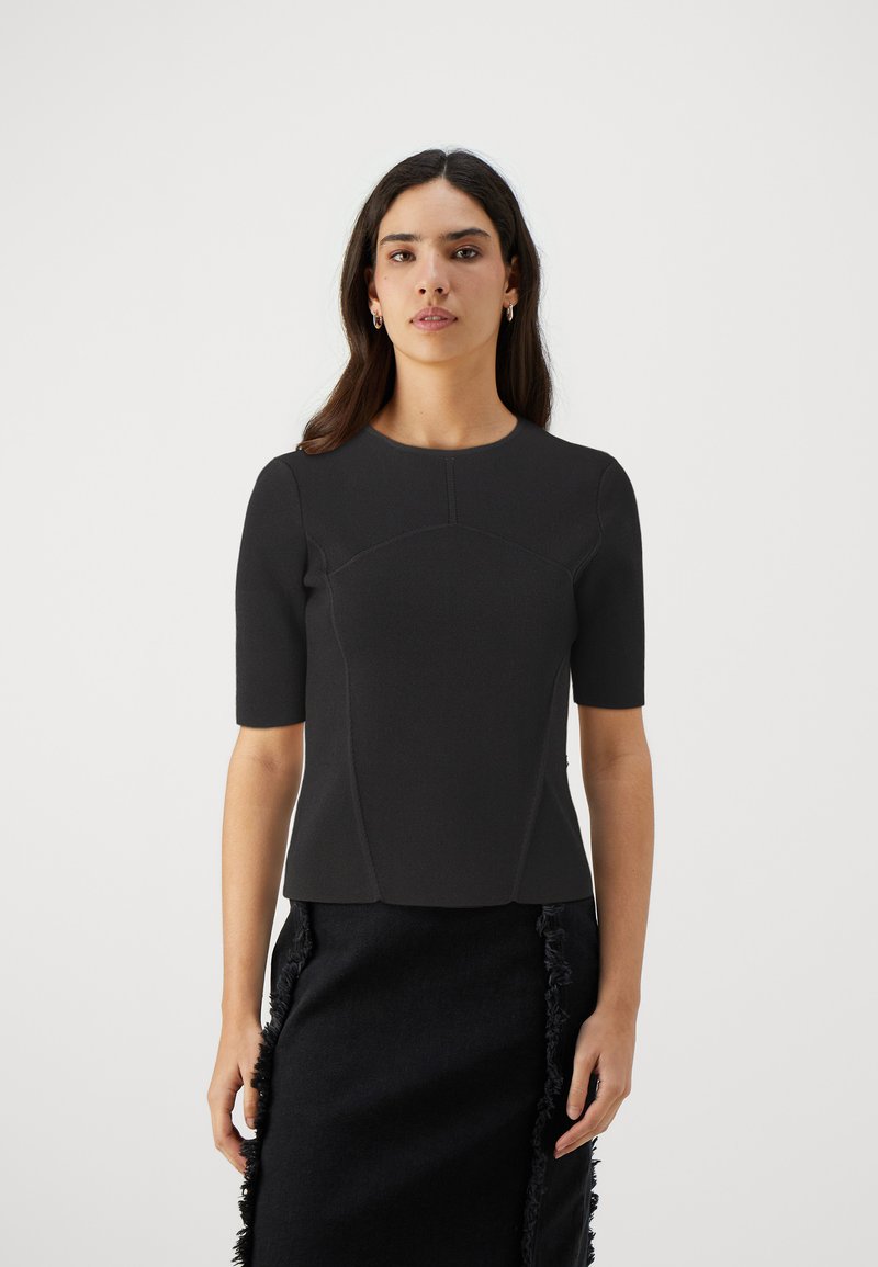 Top nero a maniche corte con un design aderente, tessuto texturizzato, scollatura tonda e cuciture che modellano il corpetto; abbinato a una gonna nera sfilacciata.