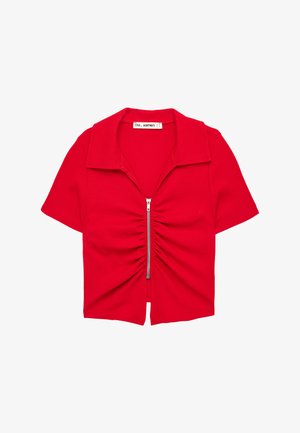 Chemise courte rouge à manches courtes avec col et fermeture éclair centrale argentée froncée à l'avant, posée à plat sur fond blanc.