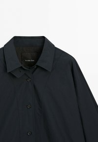 Svart knäppt kappa med spetsig krage, långa ärmar och synliga sydda sömmar, märkt Massimo Dutti.