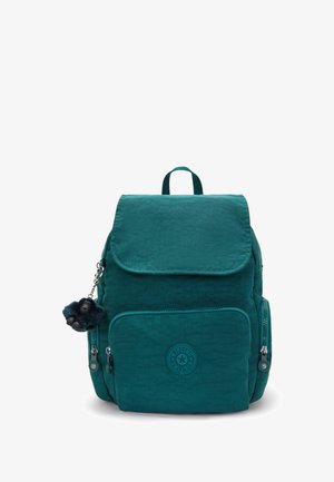 Teal backpack with a textured fabric, flap closure, front zip pocket, and a decorative monkey keychain. Features branded circular logo patch.