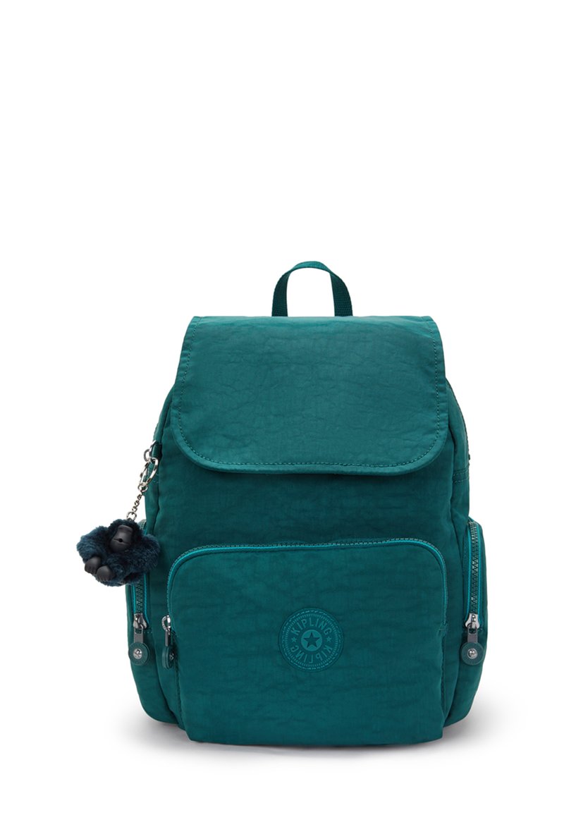 Mochila verde azulado con un tejido texturizado, cierre de solapa, bolsillo con cremallera en la parte frontal y un llavero decorativo en forma de mono. Presenta un parche circular de logo de marca.