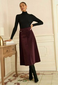 Maglione a collo alto nero a costine, maniche lunghe, abbinato a una gonna prugna fino al ginocchio con tasche frontali e bottoni argentati. Stivali neri alti fino alla coscia.