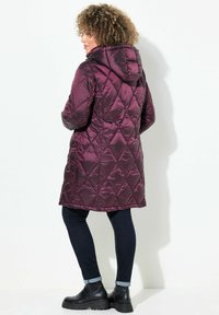 Burgundy kviltad pufferjacka med huva, med en glänsande yta, sidofickor och längd till mitten av låret, i kombination med mörka jeans och stövlar.