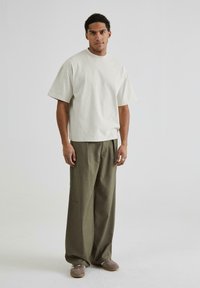 Light beige short-sleeve t-shirt, loose fit. Olive green wide-leg trousers, soft texture. Gray flat shoes with a rounded toe.
