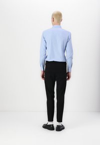 Lys blå langermet skjorte med en slim fit-design, kombinert med svarte slim-fit bukser og svarte sko med hvite sokker.